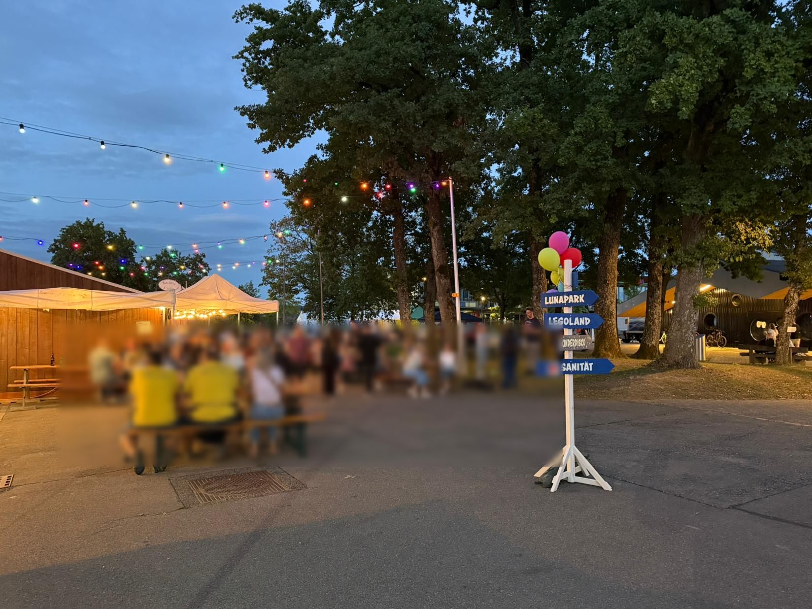 Festzelte am Abend unter Lichterketten, Gäste an langen Tischen